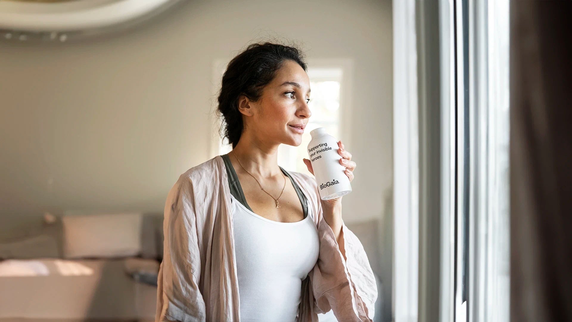 Woman looking out the window drinking water from a BioGaia probiotics water bottle